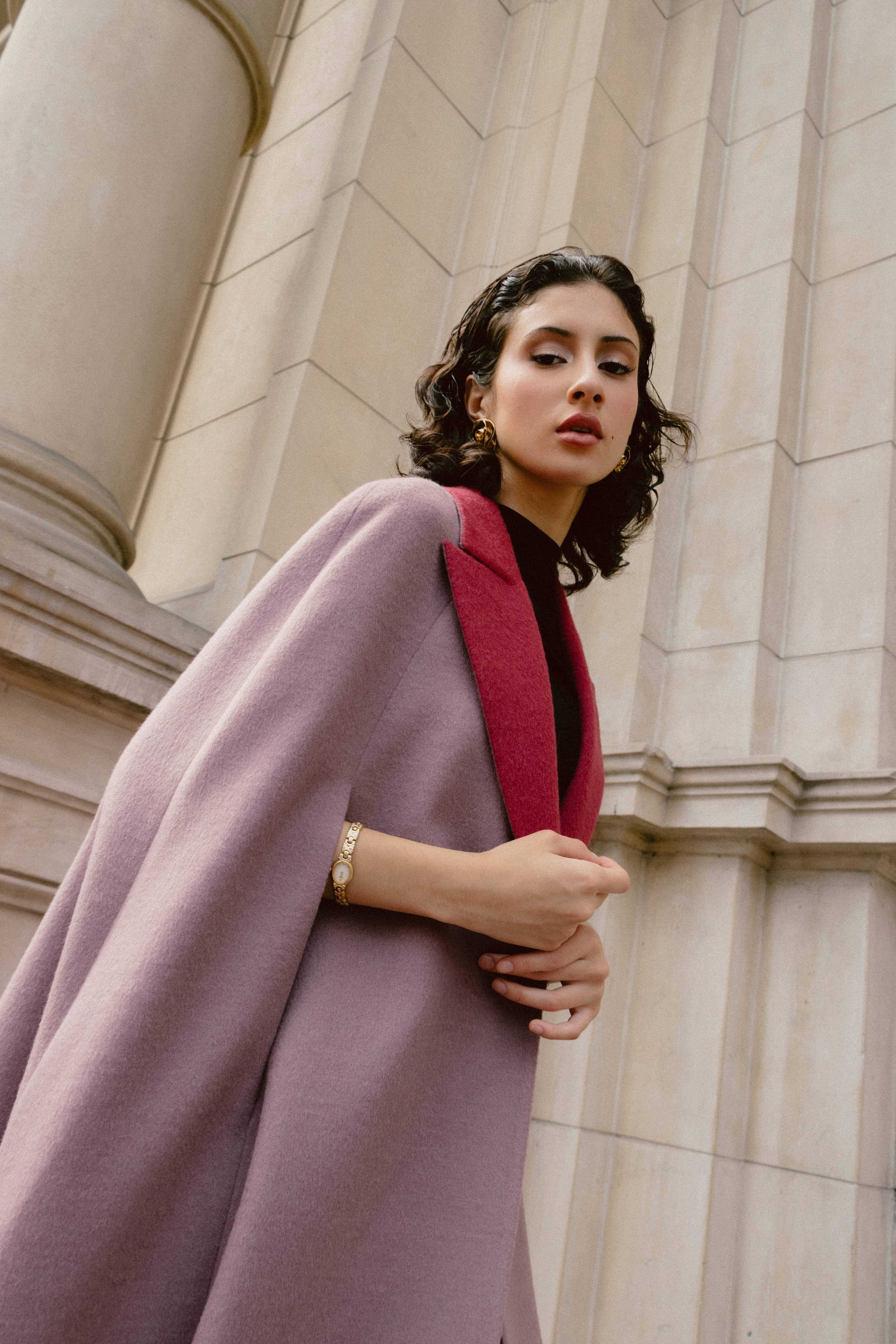A woman wearing a light purple baby alpaca cape-style coat with a red collar.