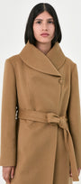 A woman wearing a camel baby alpaca coat with a wrap collar, button closure, and matching waist tie belt.
