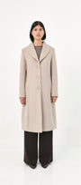 A model wearing a long, light beige baby alpaca coat with front buttons and side pockets.