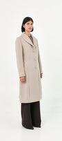 A model wearing a long, light beige baby alpaca coat with front buttons and side pockets.
