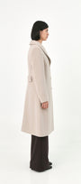 A model shown from the side profile A model wearing a long, light beige baby alpaca coat with a martingale.