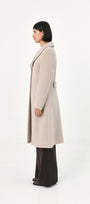 A modelstands in profile wearing a long, light beige baby alpaca coat.
