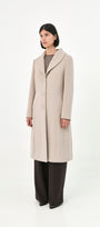 A model wearing a long, light beige  baby alpaca coat with buttons front and side pockets.