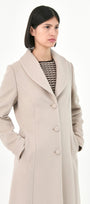 A model wearing a long, light beige  baby alpaca coat with buttons front and side pockets.