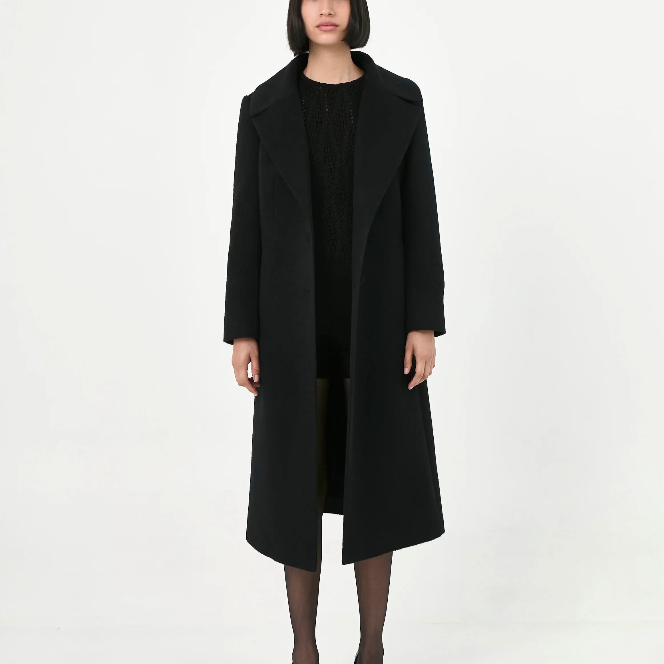 A model wearing a long black baby alpaca coat with a wide pointed lapel.