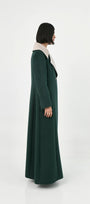 A model shown from the side profile wearing a long, dark green suri alpaca coat with a contrasting light beige collar.