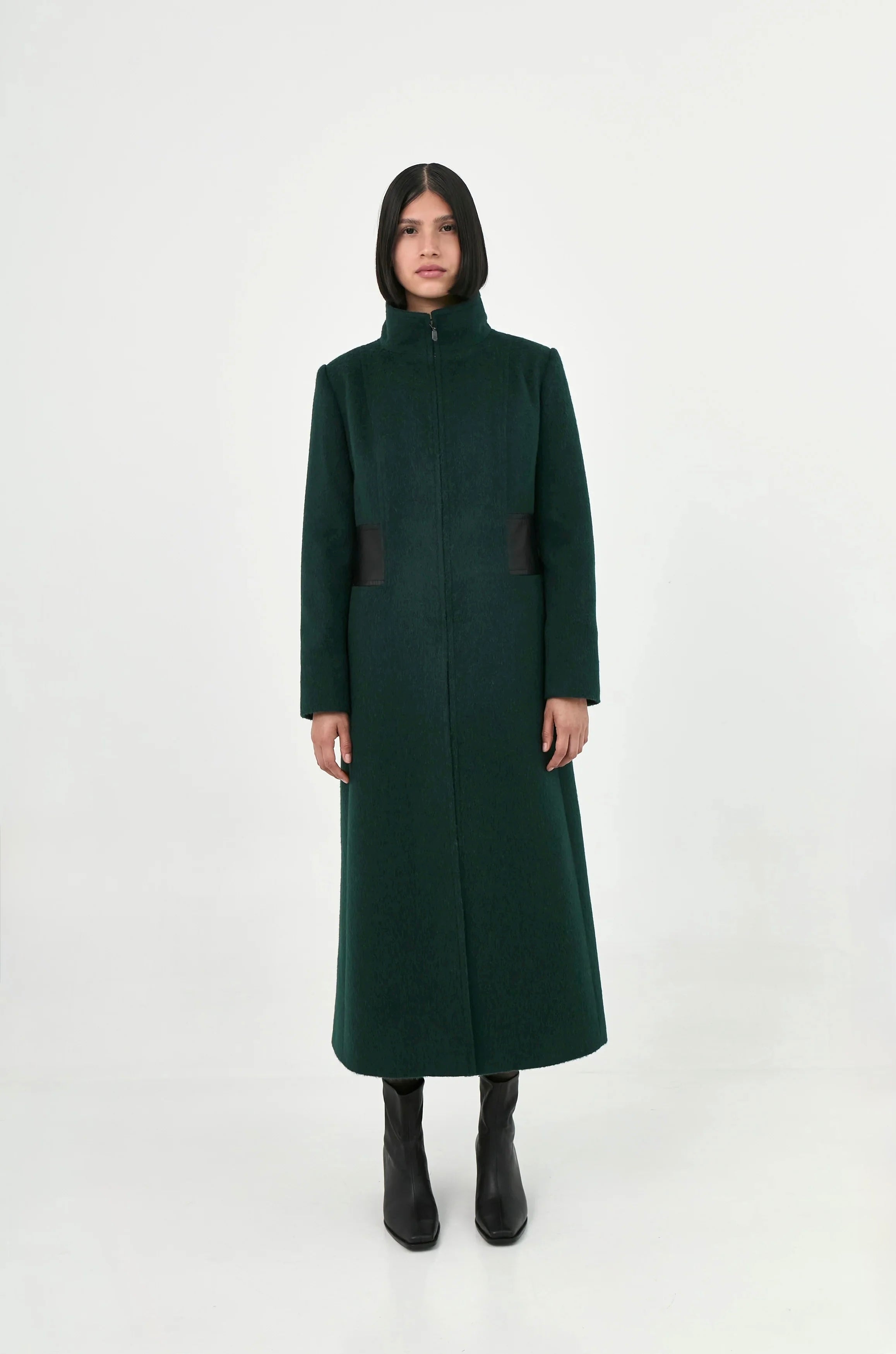 A model wearing a long, dark green baby alpaca coat with leather details.