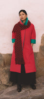 Woman wearing a fuchsia coat and patterned scarf against a stone wall.